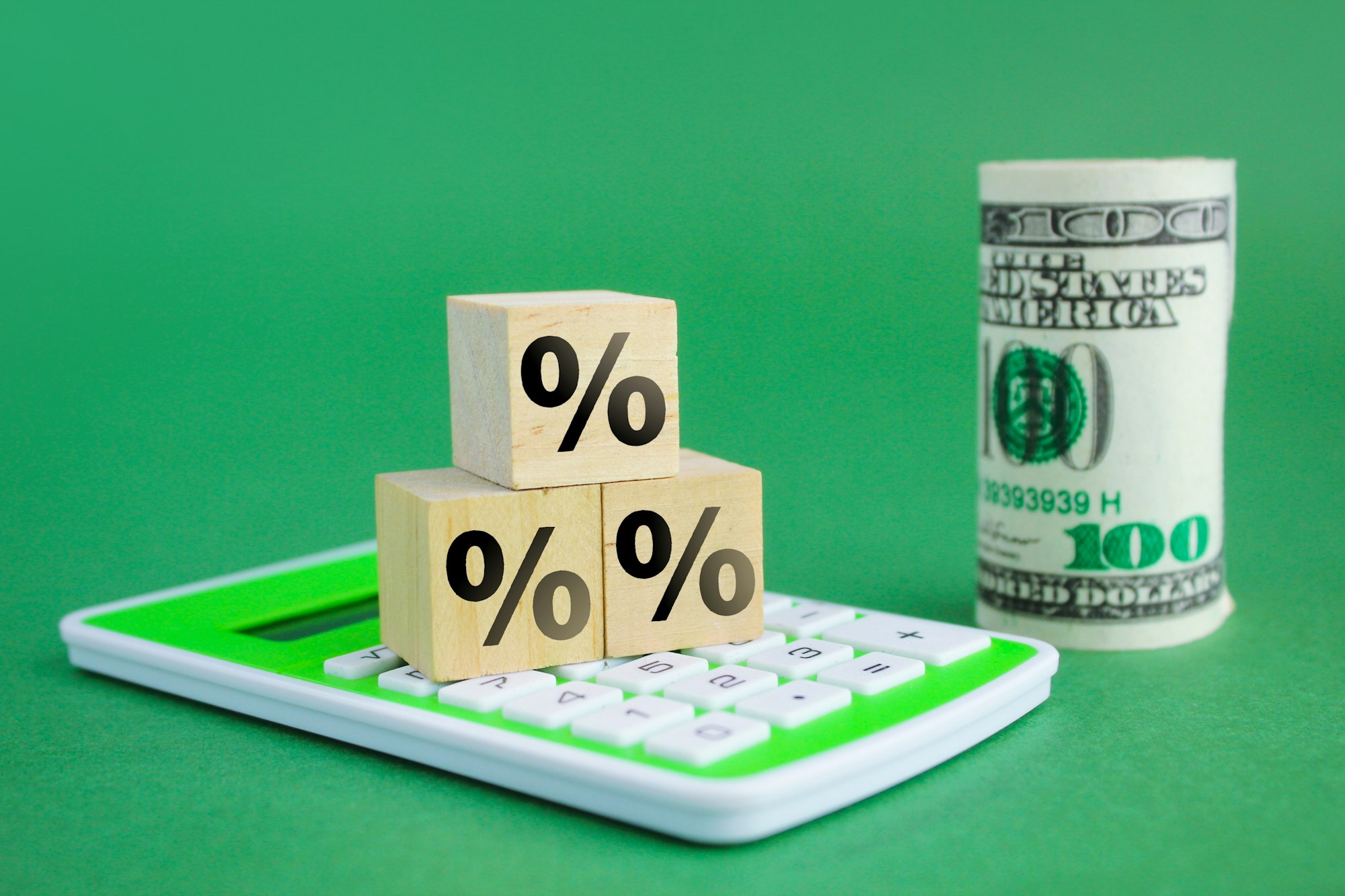 calculator, wooden cube with percent icon and a roll of money in blurred background calculator, wooden cube with percent icon and a roll of money in blurred background