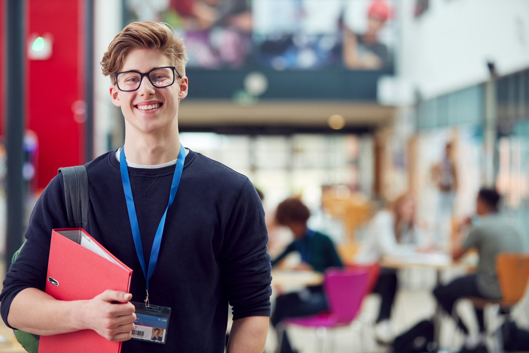 Portrait Of Smiling Male College Student In Busy Communal Campus Building Portrait Of Smiling Male College Student In Busy Communal Campus Building